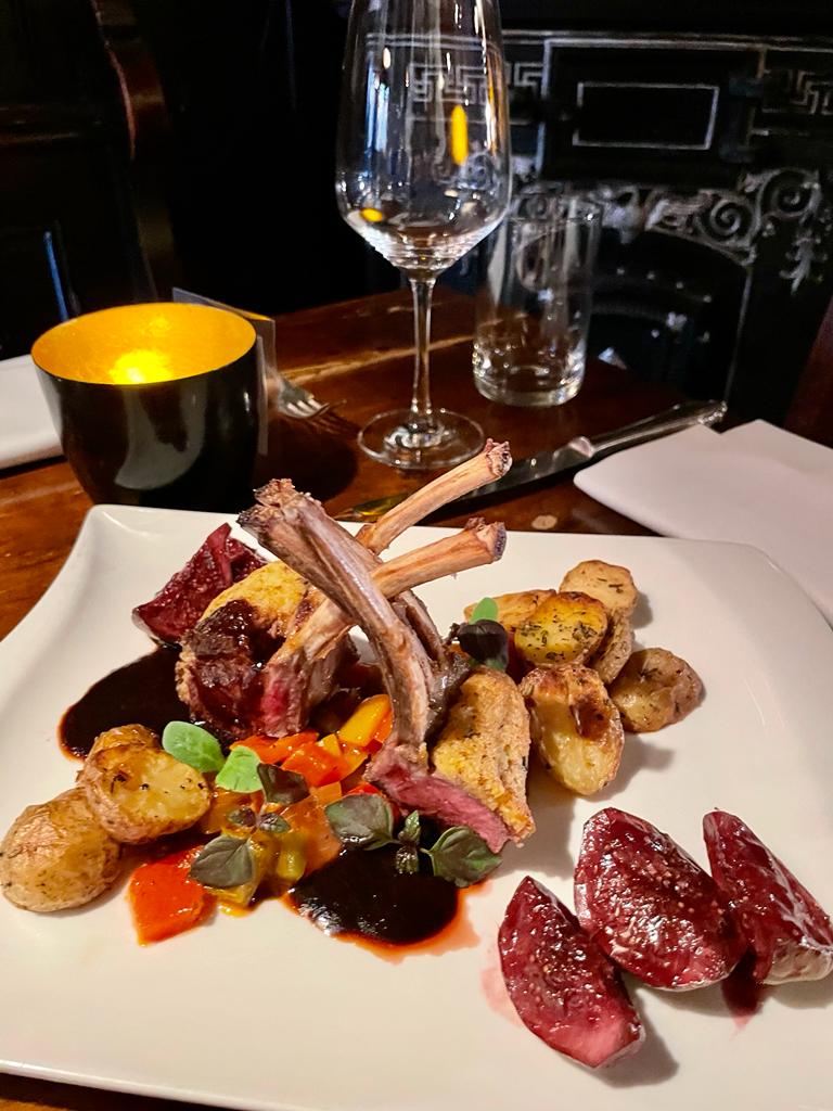 auf diesem Bild sieht man ein Teller Gericht mit gebratenem Lammkarree, dass appetitlich auf dem Teller angerichtet ist. Bei den Beilagen handelt es sich um buntes Gem&uuml;se sowie ger&ouml;stete Rosmarin Kartoffeln.